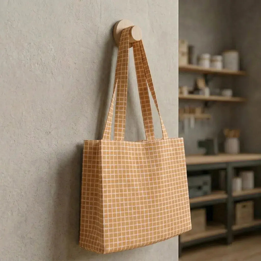 grand sac cabas en coton enduit à carreaux beige suspendu contre un mur