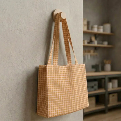 grand sac cabas en coton enduit à carreaux beige suspendu contre un mur