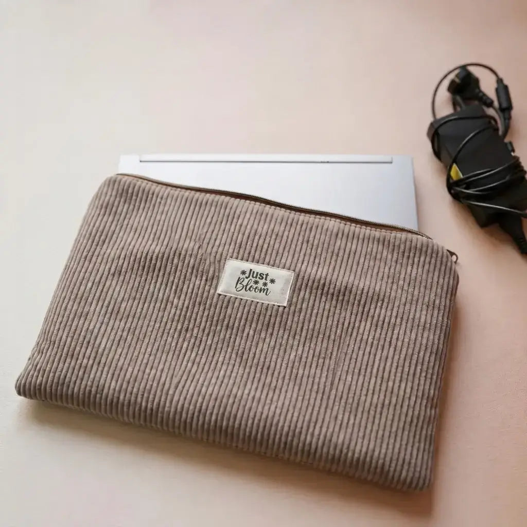Housse zippée pour ordinateur portable en velours côtelé taupe, étiquette Just Bloom et chargeur à côté
