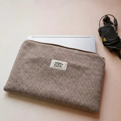Housse zippée pour ordinateur portable en velours côtelé taupe, étiquette Just Bloom et chargeur à côté