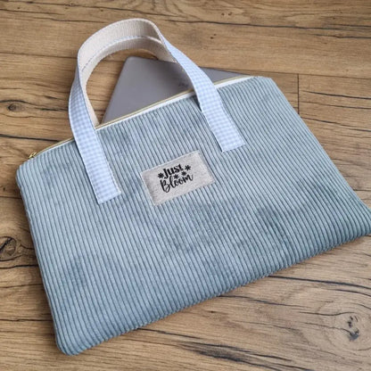 Housse pour iPad ou tablette tactile en velours côtelé bleu clair avec poignée décorée par un tissu au motif carreaux bleus. Cette housse est personnalisée avec une étiquette en tissu couleur lin floquée avec l'inscription "Just Bloom" en noir.