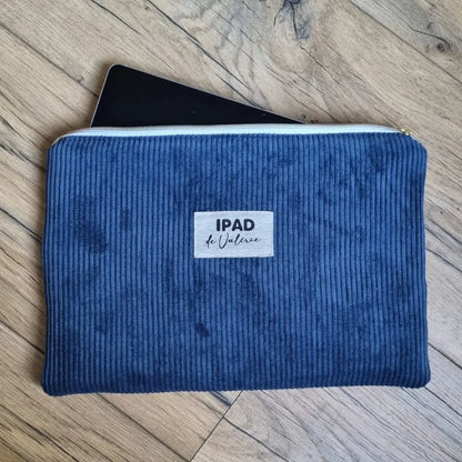 Housse pour iPad ou tablette tactile en velours côtelé de coloris bleu foncé. Cette housse est personnalisée avec l'inscription "IPAD de Valérie" floquée en son centre sur une étiquette en tissu. Une tablette dépasse légèrement de la housse par son ouverture zippée.