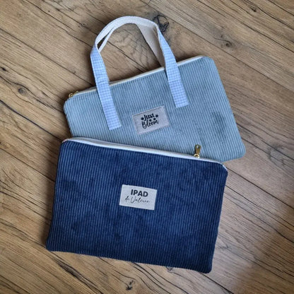 En haut, une housse pour iPad ou tablettes tactiles en velours côtelé bleu clair munie de poignées doublées avec un coton imprimé à motif carreaux bleus. Cette housse est personnalisée avec l'inscription "Just Bloom". En bas, la même housse mais en velours côtelé bleu foncé et sans poignée. Celle-ci est personnalisée avec l'inscription "iPad de Céline".