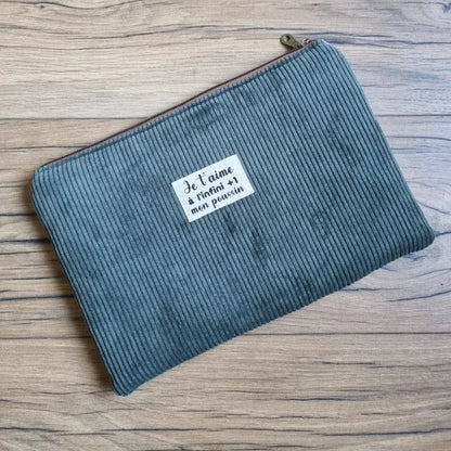 Housse pour iPad ou tablette en velours côtelé vert, fermée par un zip métallique sur le dessus et ornée d’une étiquette floquée au message 'Je t’aime à l’infini +1 mon poussin'. Élégante et pratique, cette pochette protège vos appareils des rayures et chocs tout en ajoutant une touche personnalisée et chaleureuse, idéale pour un cadeau unique ou un accessoire du quotidien.