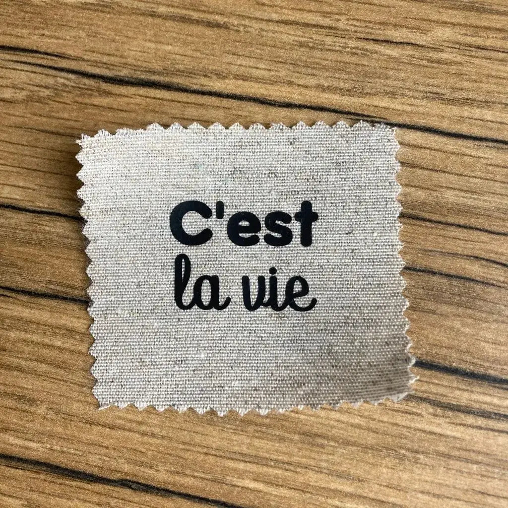 Inscription personnalisée "C'est la vie" floquée en flex thermocollant sur une étiquette en tissu.