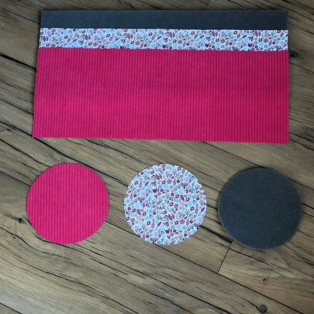 Kit couture corbeille : velours côtelé fuchsia, tissu Liberty floral et disques de mousse sur sol boisé.