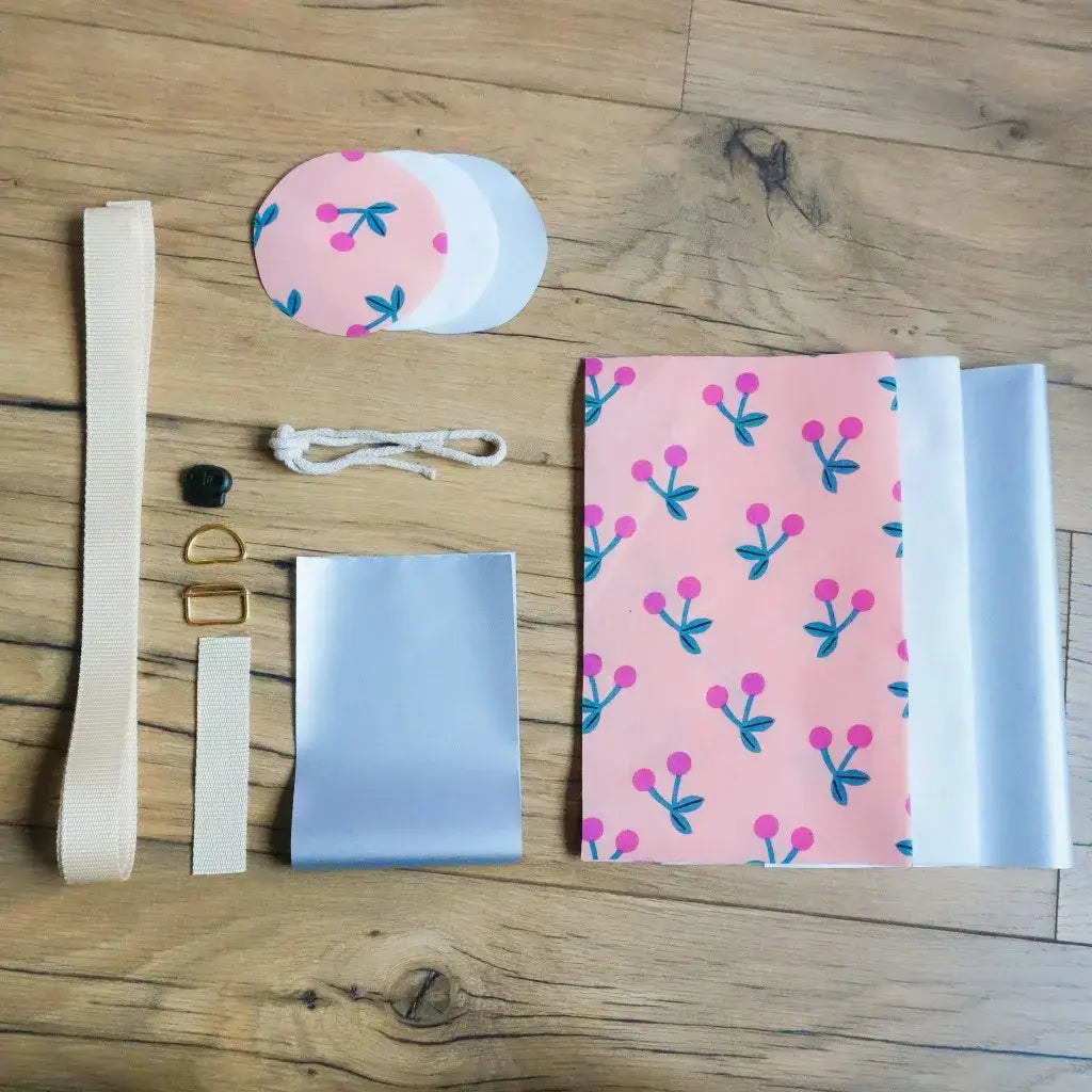 Kit couture complet porte-gourde motif cerise sur fond rose : coton enduit fruité, isolant thermique, sangle beige et mercerie dorée.
