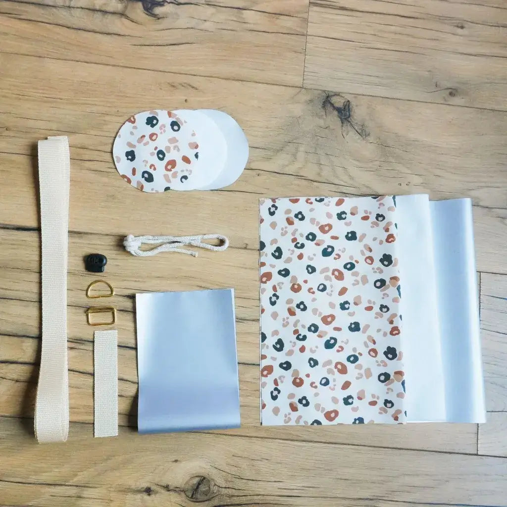 Kit couture DIY porte-gourde isotherme motif léopard : coton enduit à taches fauves, isolant thermique blanc, sangle beige et mercerie dorée.