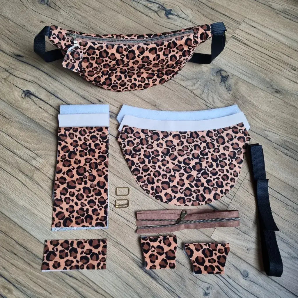 Sac demi-lune léopard fini et ses pièces de kit couture : tissus, ouatine, sangle et zip sur plan de travail en bois.