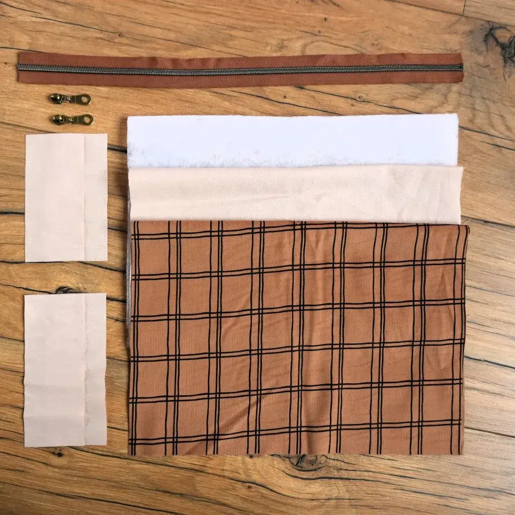 Kit couture prêt-à-coudre pour confectionner une trousse carrée à motif carreaux camel et noir, comprenant toutes les pièces nécessaires : tissu principal, doublure, renfort en ouate, fermeture éclair marron et curseurs métalliques. Ensemble idéal pour les amateurs de DIY souhaitant réaliser une trousse personnalisée élégante, pratique et moderne, parfaite pour ranger maquillage, accessoires de voyage ou produits de beauté.