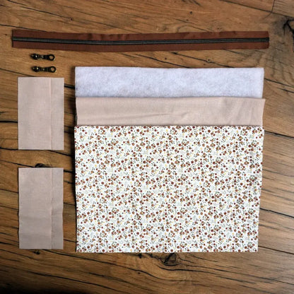 Kit couture complet pour réaliser une trousse carrée à motif fleuri façon prairie, composé du tissu principal à petites fleurs, d’une doublure beige, de pièces de ouate, d’une fermeture éclair marron et de deux curseurs métalliques. Ce kit prêt-à-coudre permet de fabriquer facilement une trousse personnalisée au style champêtre, idéale pour offrir ou organiser ses accessoires de toilette.