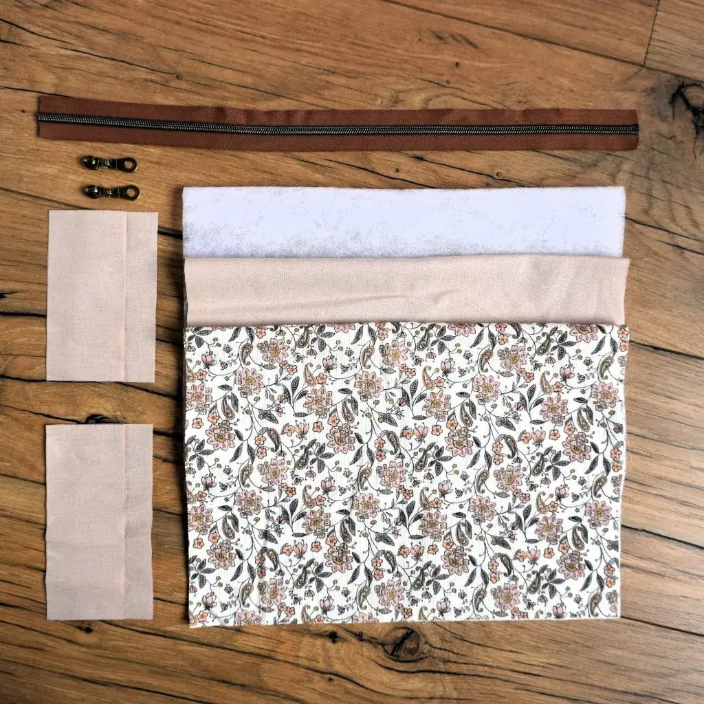 Kit couture DIY pour créer une trousse carrée à motif fleuri beige et terracotta, composé du tissu principal imprimé, d’une doublure unie, de ouate, d’une fermeture éclair marron et de deux curseurs en métal. Ce kit prêt-à-coudre est idéal pour les couturières souhaitant réaliser un accessoire raffiné et unique, parfait pour ranger maquillage, fournitures ou petits objets du quotidien.