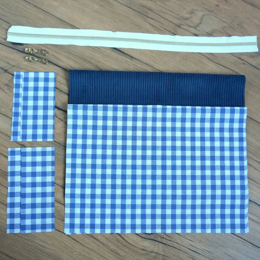 Kit couture prêt-à-coudre pour créer une trousse carrée en tissu vichy bleu et blanc, associée à un empiècement en velours côtelé bleu marine. Le lot comprend également une fermeture éclair écrue et deux curseurs métalliques dorés. Facile à assembler, ce kit DIY permet de réaliser une trousse artisanale au style classique et intemporel, idéale pour le rangement ou comme idée cadeau personnalisée.