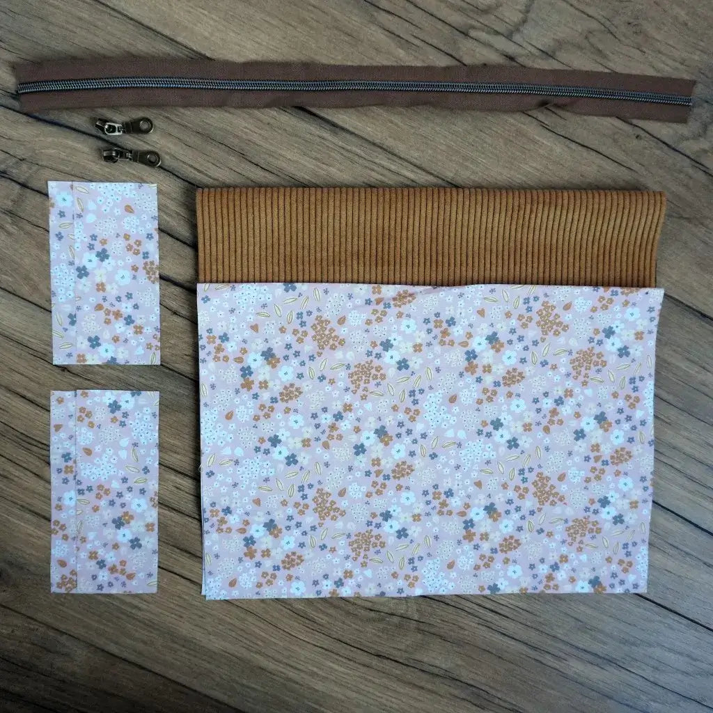 Kit couture prêt-à-coudre pour confectionner une trousse carrée chic, mêlant un velours côtelé jaune et un tissu fleuri aux teintes douces de beige, gris et terracotta. Le kit comprend une fermeture éclair marron et deux curseurs métalliques assortis. Facile à réaliser, il permet de créer une trousse unique et élégante, idéale pour ranger ses affaires ou offrir un cadeau fait main personnalisé.