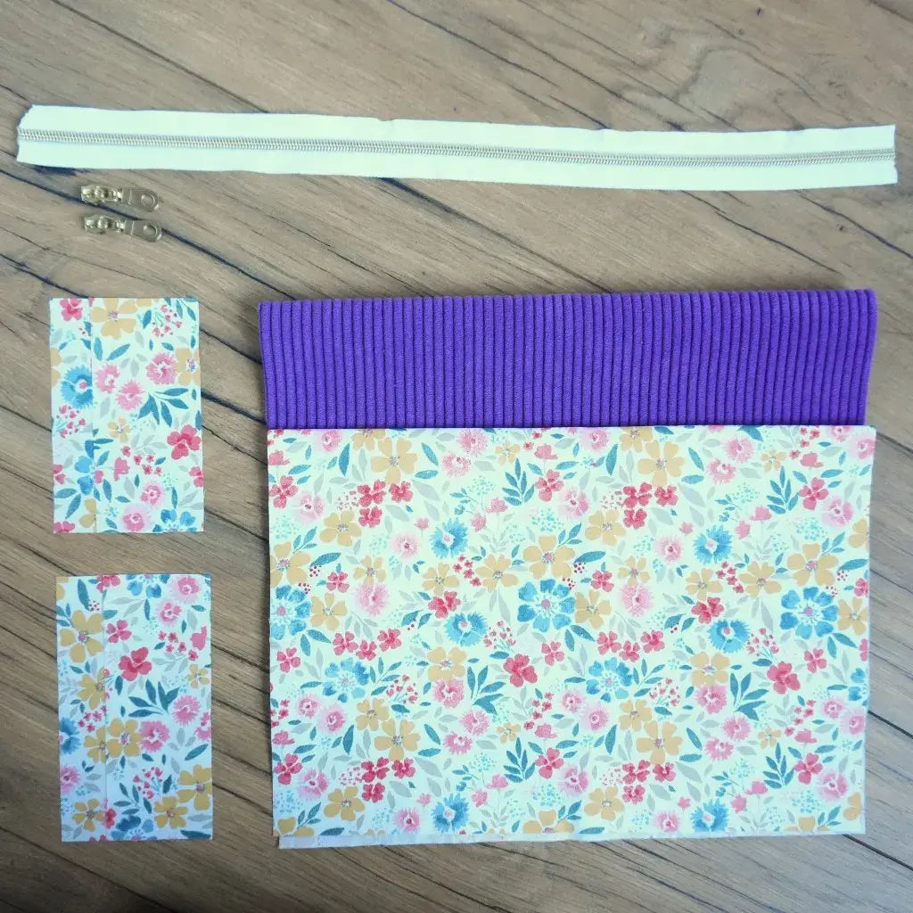 Kit couture complet pour créer une trousse carrée colorée, associant un velours côtelé violet intense et un tissu fleuri lumineux aux tons jaune, bleu et rose. Il comprend une fermeture éclair écrue et deux curseurs dorés. Idéal pour un projet DIY printanier, ce kit prêt-à-coudre permet de confectionner une trousse artisanale pleine de pep’s, parfaite pour ranger accessoires, maquillage ou petits trésors.