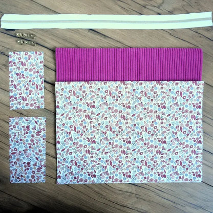 Kit couture DIY pour confectionner une trousse carrée élégante, mariant un velours côtelé magenta éclatant à un tissu fleuri type liberty. Ce kit comprend une fermeture éclair blanche, deux curseurs métalliques dorés et toutes les pièces pré-découpées. Parfait pour un projet créatif rapide et tendance, il permet de réaliser une trousse personnalisée aussi pratique que décorative.