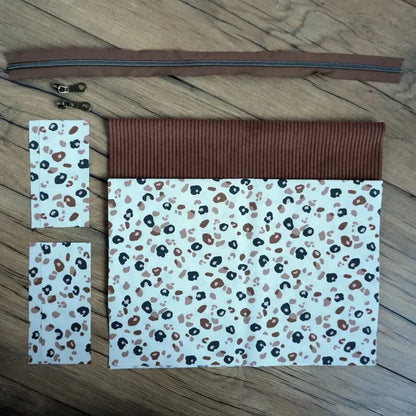 Kit couture complet pour réaliser une trousse carrée tendance, combinant un velours côtelé brun chaud et un tissu à imprimé léopard beige, noir et terracotta. Livré avec une fermeture éclair marron et deux curseurs métalliques, ce kit prêt-à-coudre offre un projet simple et moderne. Idéal pour les amateurs de couture souhaitant créer une trousse originale au style animal et élégant.