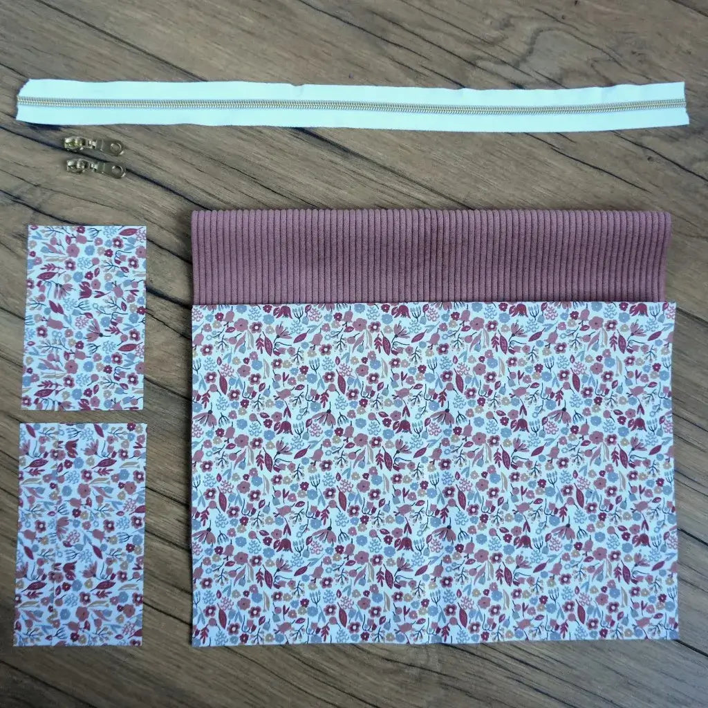 Kit couture complet pour réaliser une trousse carrée douce et féminine, composée d’un velours côtelé rose poudré et d’un tissu fleuri aux nuances de mauve, rouge et gris type liberty. Le kit inclut une fermeture éclair blanche, deux curseurs dorés et les pièces de tissu assorties. Facile à coudre, ce projet DIY allie charme et praticité pour créer une trousse unique à offrir ou à s’offrir.