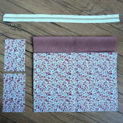 Kit couture complet pour réaliser une trousse carrée douce et féminine, composée d’un velours côtelé rose poudré et d’un tissu fleuri aux nuances de mauve, rouge et gris type liberty. Le kit inclut une fermeture éclair blanche, deux curseurs dorés et les pièces de tissu assorties. Facile à coudre, ce projet DIY allie charme et praticité pour créer une trousse unique à offrir ou à s’offrir.