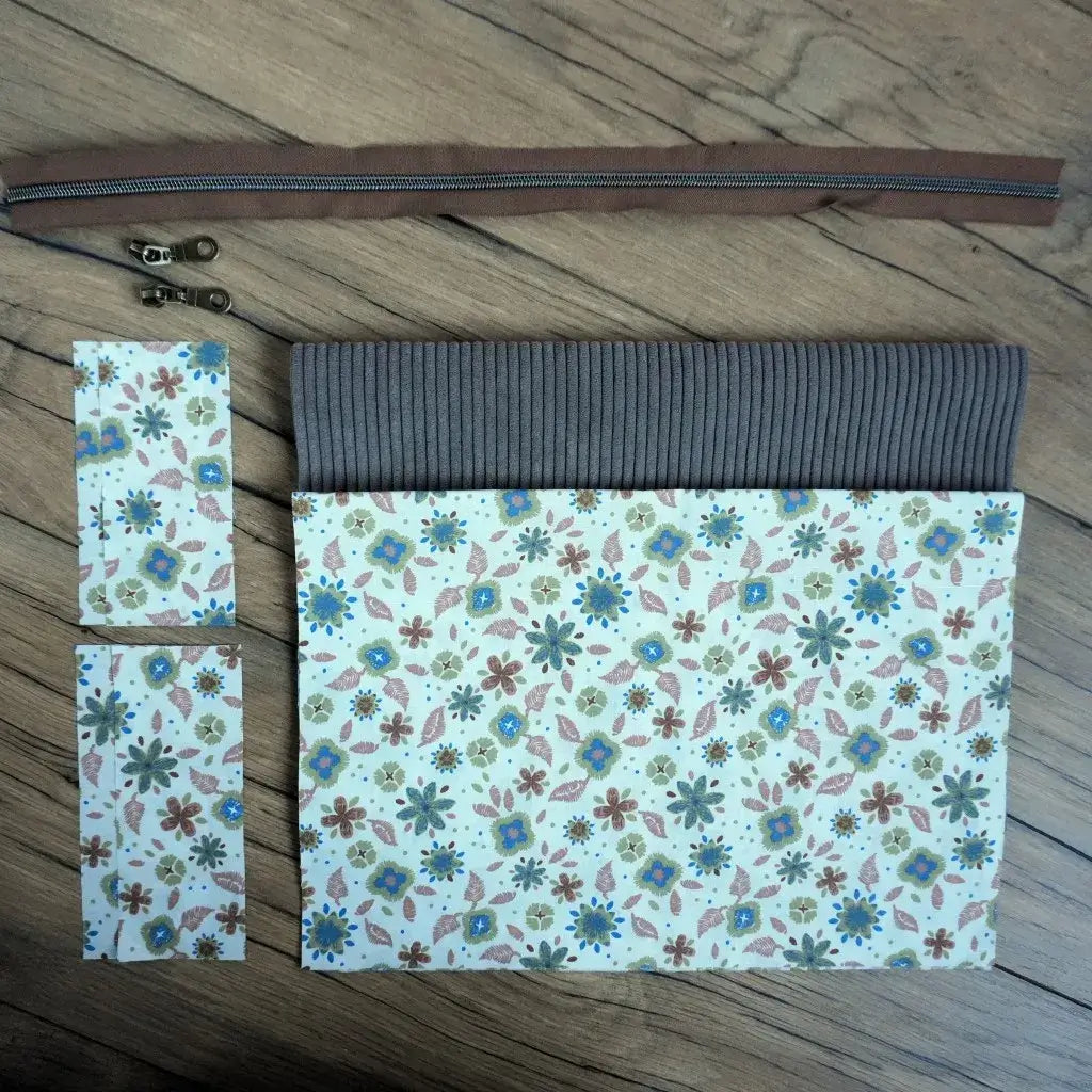 Kit couture prêt-à-coudre pour confectionner une trousse carrée harmonieuse, mariant un velours côtelé taupe élégant à un tissu fleuri dans des tons de bleu, vert et beige. Le kit comprend une fermeture éclair marron, deux curseurs métalliques et les éléments textiles assortis. Facile à réaliser, ce projet DIY permet de créer une trousse artisanale chic et naturelle, idéale pour offrir ou organiser ses accessoires.