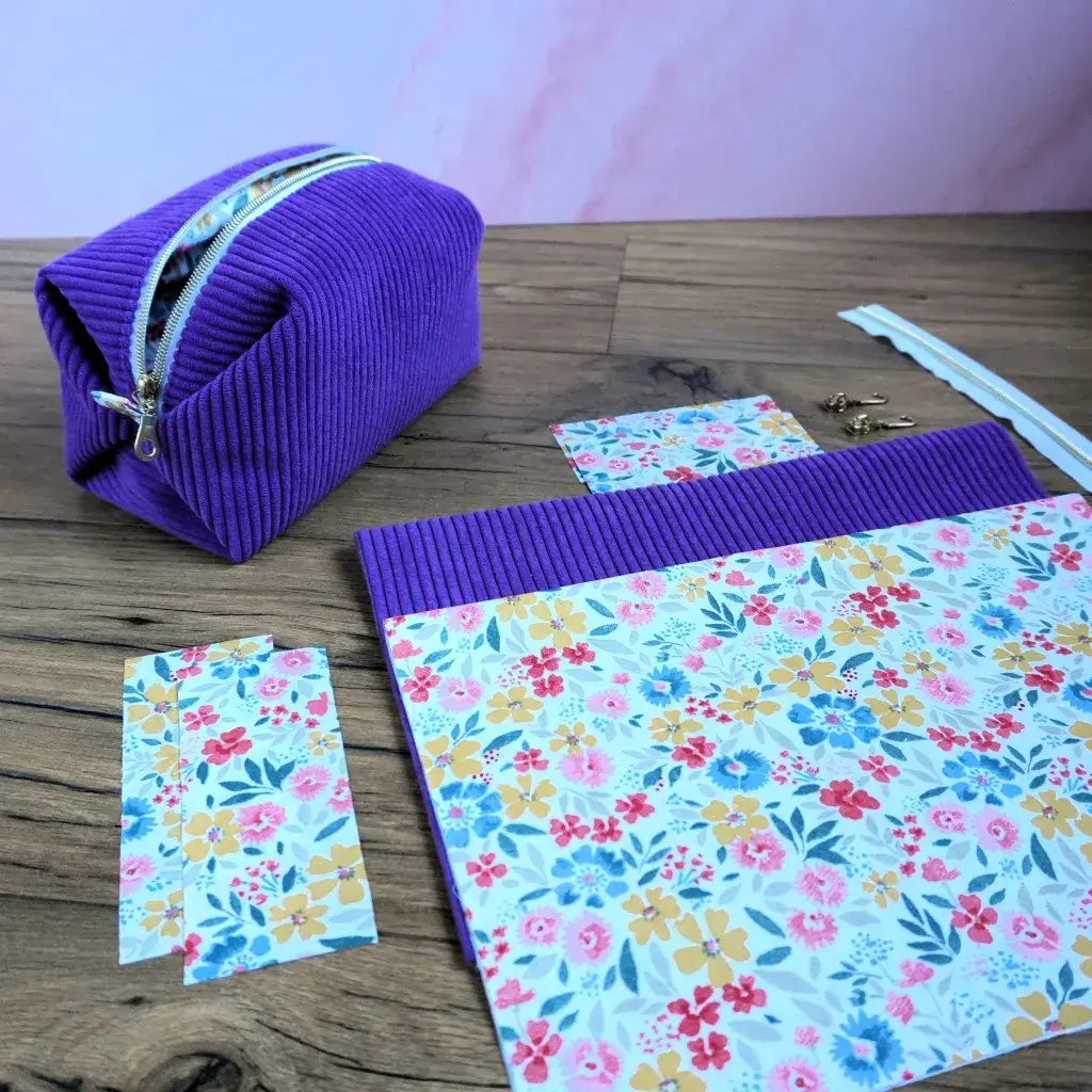 Trousse carrée en velours côtelé lavande réalisée à la main, accompagnée des pièces de tissu fleuri prêtes à coudre, d’une fermeture éclair et d’accessoires métalliques dorés. Ce kit couture complet permet de confectionner une trousse élégante et personnalisée, alliant la douceur du velours et la fraîcheur d’un motif floral coloré. Idéal pour les passionnés de couture ou les idées cadeaux fait main.