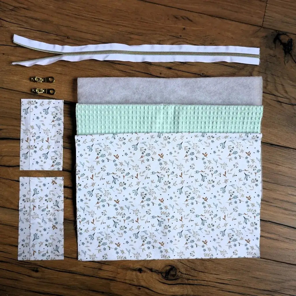 Kit prêt-à-coudre pour réaliser une trousse carrée en nid d’abeille vert menthe, accompagnée d’une doublure en coton fleuri aux motifs délicats. Le kit comprend tous les éléments nécessaires : tissus, ouate, fermeture éclair blanche dorée et curseurs métalliques. Parfait pour un projet de couture printanier et tendance, accessible aux débutants comme aux passionnés de fait main.
