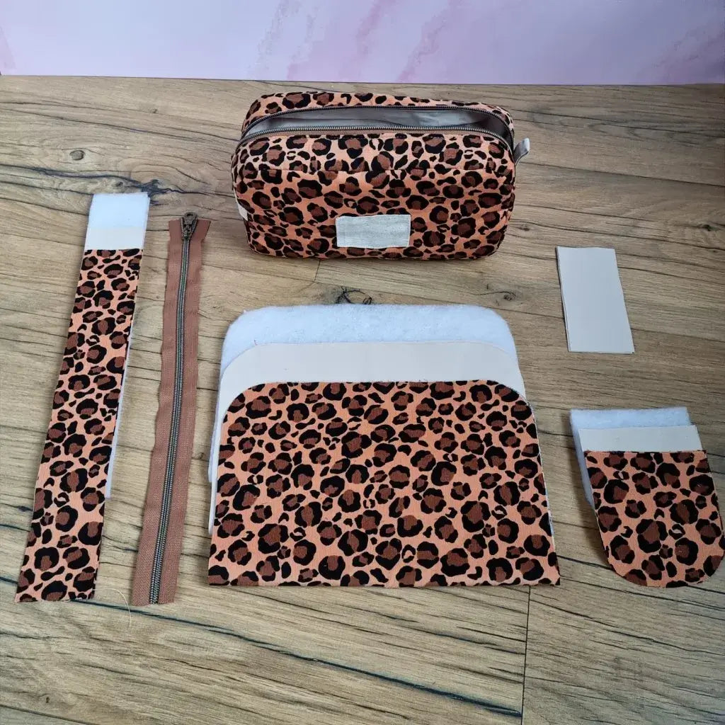 Kit couture et sa trousse de toilette léopard finie : coupons velours, ouatine, zip et doublure sur fond bois.