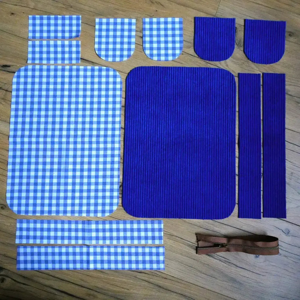 Pièces de tissu en velours bleu et vichy découpées sur un parquet avec une fermeture éclair pour coudre une trousse.