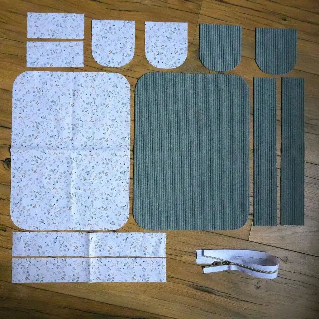 Kit couture : coupons de velours côtelé vert lichen et tissu fleuri minimaliste avec zip blanc sur parquet.