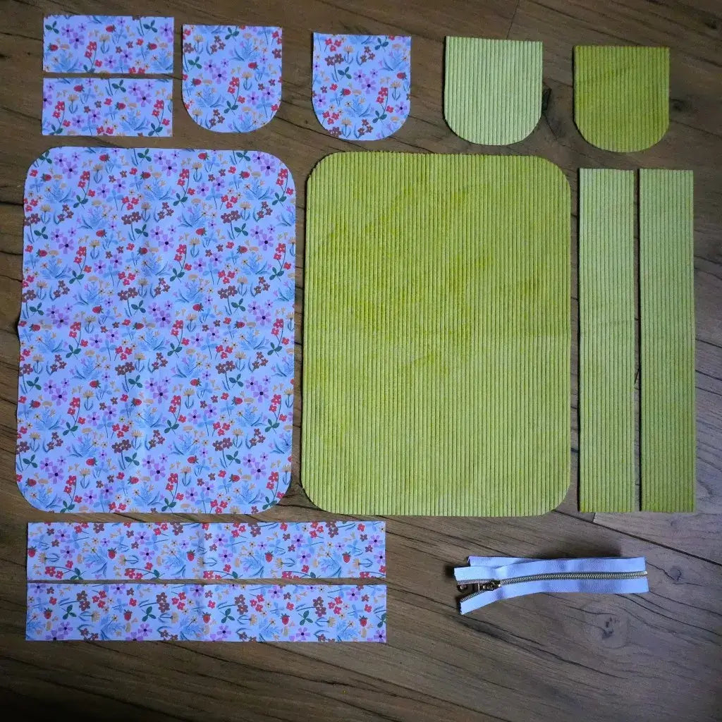 Kit couture : pièces en velours côtelé vert anis et tissu fleuri printanier avec zip blanc sur fond bois.
