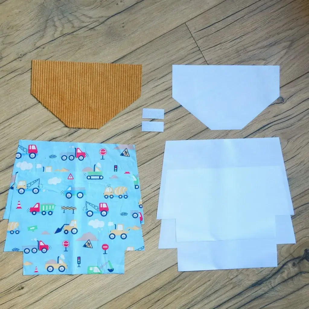 Kit couture prêt-à-coudre pour réaliser une pochette à scratch imperméable, comprenant un rabat en velours côtelé couleur moutarde, des coupons de coton bleu clair imprimé avec motifs engins de chantier, véhicules et panneaux, ainsi que doublures blanches et scratchs assortis. Parfait pour créer une trousse originale et personnalisée, ce kit DIY est idéal pour initier les enfants à la couture ou offrir un cadeau fait main unique.