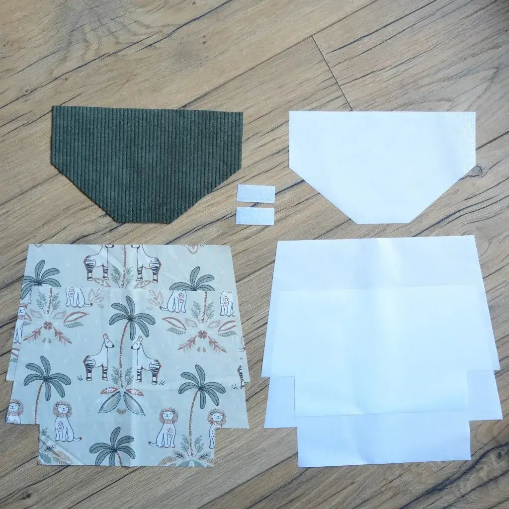 Kit couture prêt-à-coudre pour fabriquer une pochette à scratch imperméable, avec un rabat en velours côtelé vert, des coupons de coton imprimé jungle représentant lions, zèbres et palmiers, des doublures blanches en coton enduit et des scratchs. Un projet DIY créatif pour réaliser une trousse pratique et originale, parfaite pour les enfants et idéale comme cadeau fait main personnalisé.