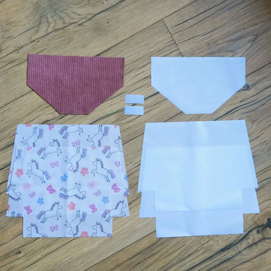 Kit couture prêt-à-coudre pour réaliser une pochette à scratch imperméable, comprenant un rabat en velours côtelé rose, des coupons de coton blanc imprimé de licornes colorées, fleurs et papillons, des doublures blanches ainsi que deux scratchs. Ce kit DIY ludique et complet permet de créer une trousse personnalisée et magique, parfaite pour les enfants et idéale comme cadeau fait main.