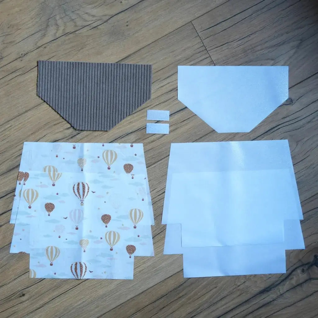 Kit couture DIY pour confectionner une pochette à scratch imperméable, comprenant un rabat en velours côtelé taupe, des coupons de coton blanc imprimé de montgolfières dans des tons beige et brun, des doublures blanches en coton enduit et deux scratchs. Ce kit prêt-à-coudre complet permet de réaliser une trousse personnalisée, originale et résistante, parfaite comme projet créatif ou cadeau fait main.