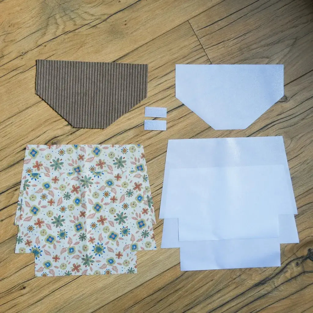 Kit couture DIY pour confectionner une pochette à scratch imperméable, comprenant un rabat en velours côtelé taupe, des coupons de coton imprimé floral aux tons colorés vert, bleu et rouge, des doublures blanches en coton enduit et deux scratchs. Ce kit prêt-à-coudre complet permet de créer une trousse unique et pratique, idéale pour un projet créatif ou comme cadeau fait main personnalisé.