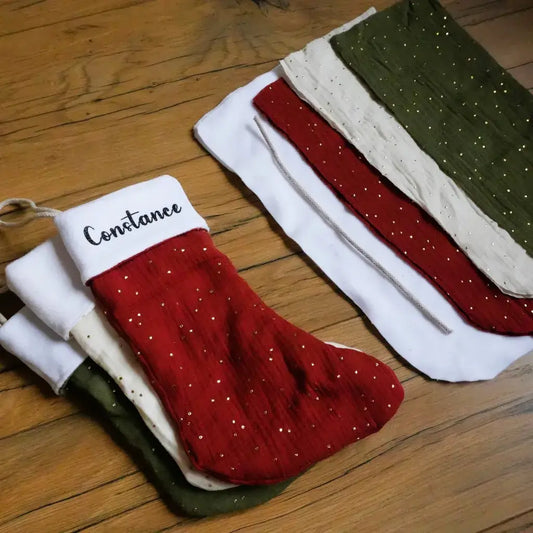 Botte de Noël en double gaze de coton scintillante, cousue main et personnalisable avec le prénom de l’enfant. Trois coloris festifs disponibles : rouge, vert sapin et écru à pois dorés. Idéale pour suspendre au pied du sapin et glisser des petites attentions. Fabrication artisanale française, parfaite pour une décoration de Noël naturelle et chaleureuse.