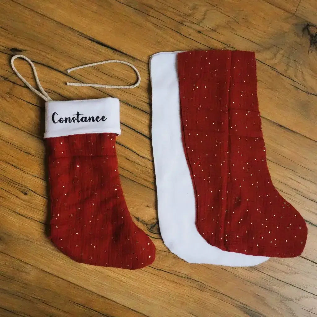 Kit couture pour créer une botte de Noël rouge en double gaze de coton parsemée de paillettes dorées. Le kit comprend toutes les pièces nécessaires : tissu extérieur, doublure polaire blanche et cordon d’attache. Possibilité de personnaliser le revers avec un prénom. Un projet DIY idéal pour une décoration de Noël artisanale, élégante et faite main, à suspendre près du sapin ou de la cheminée.