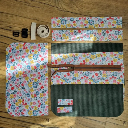Kit prêt-à-coudre pour réaliser un tablier-ceinture comprenant toutes les pièces de tissu prédécoupées en velours côtelé vert et coton imprimé floral multicolore, une fermeture éclair, une sangle et des accessoires de bouclerie. Parfait pour les projets DIY couture. Ce tablier-ceinture est idéal pour les activités créatives ou pour offrir à des maîtresses, nounous, ATSEM... et est personnalisable avec un prénom ou une inscription au choix.