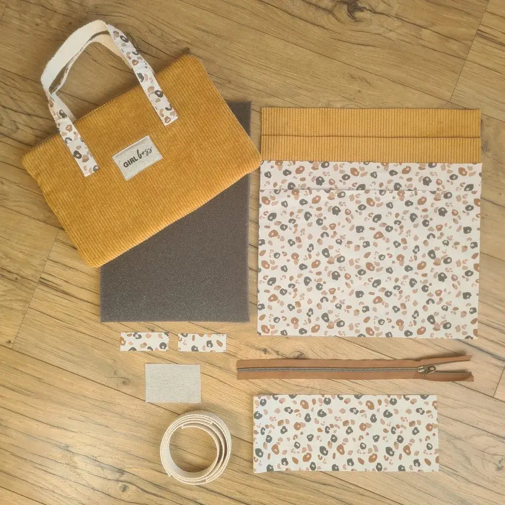 Kit "prêt à coudre" pour réaliser une housse avec anses pour tablette ou iPad en velours côtelé jaune doublée avec un tissu à motif léopard. Ce kit couture est composé de 2 plaques en mousse, de 2 pièces en velours côtelé jaune, de 5 pièces en coton imprimé à motif léopard, d'une fermeture éclair marron et de 2 sangles. La housse est personnalisable avec un prénom ou une inscription qui peut être floquée sur une étiquette en tissu coton et lin. En haut à gauche est présenté le produit fini.