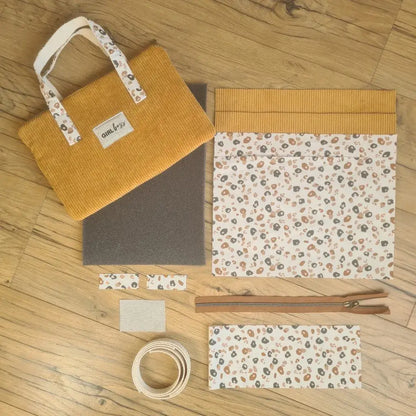 Kit "prêt à coudre" pour réaliser une housse avec anses pour tablette ou iPad en velours côtelé jaune doublée avec un tissu à motif léopard. Ce kit couture est composé de 2 plaques en mousse, de 2 pièces en velours côtelé jaune, de 5 pièces en coton imprimé à motif léopard, d'une fermeture éclair marron et de 2 sangles. La housse est personnalisable avec un prénom ou une inscription qui peut être floquée sur une étiquette en tissu coton et lin. En haut à gauche est présenté le produit fini.