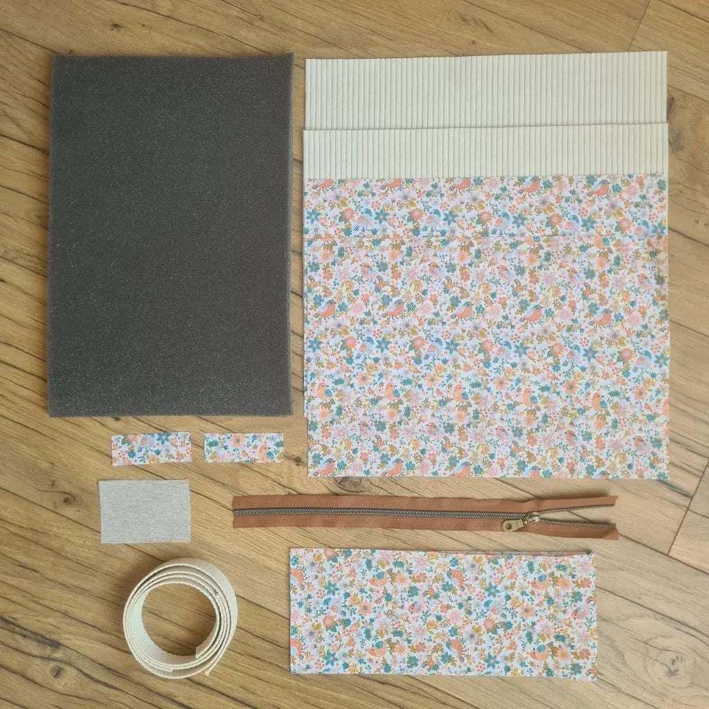 Kit "prêt à coudre" pour réaliser une housse avec anses pour tablette ou iPad en velours côtelé beige doublée avec un tissu à motif oiseaux et fleurs. Ce kit couture est composé de 2 plaques en mousse, de 2 pièces en velours côtelé beige, de 5 pièces en coton imprimé à motif oiseaux et fleurs, d'une fermeture éclair marron et de 2 sangles. La housse est personnalisable avec un prénom ou une inscription qui peut être floquée sur une étiquette en tissu coton et lin.