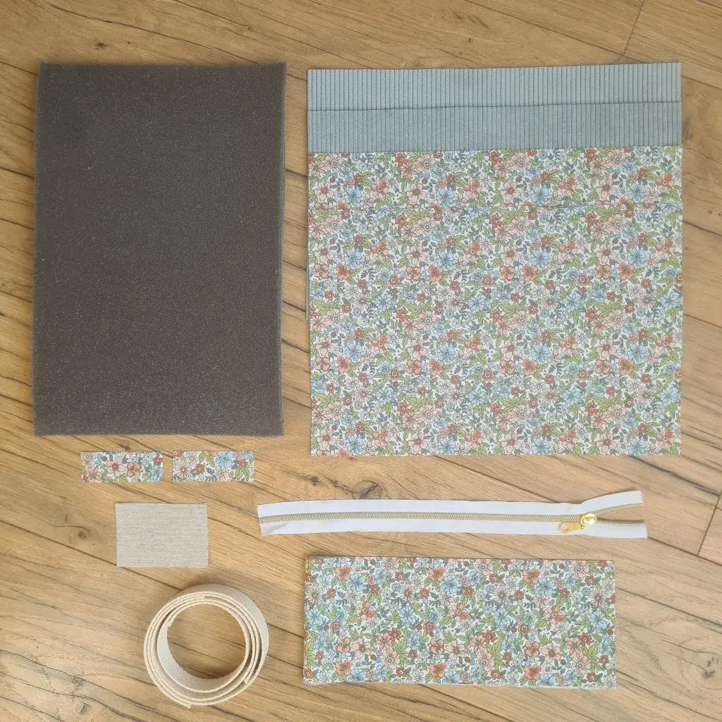 Kit "prêt à coudre" pour réaliser une housse avec anses pour tablette ou iPad en velours côtelé bleu clair doublée avec un tissu à motif fleurs. Ce kit couture est composé de 2 plaques en mousse, de 2 pièces en velours côtelé bleu clair, de 5 pièces en coton imprimé à motif fleurs, d'une fermeture éclair blanche et de 2 sangles. La housse est personnalisable avec un prénom ou une inscription qui peut être floquée sur une étiquette en tissu coton et lin.
