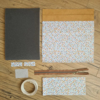 Kit "prêt à coudre" pour réaliser une housse avec anses pour tablette ou iPad en velours côtelé jaune doublée avec un tissu à motif fleurette. Ce kit couture est composé de 2 plaques en mousse, de 2 pièces en velours côtelé jaune, de 5 pièces en coton imprimé à motif fleurette, d'une fermeture éclair marron et de 2 sangles. La housse est personnalisable avec un prénom ou une inscription qui peut être floquée sur une étiquette en tissu coton et lin.