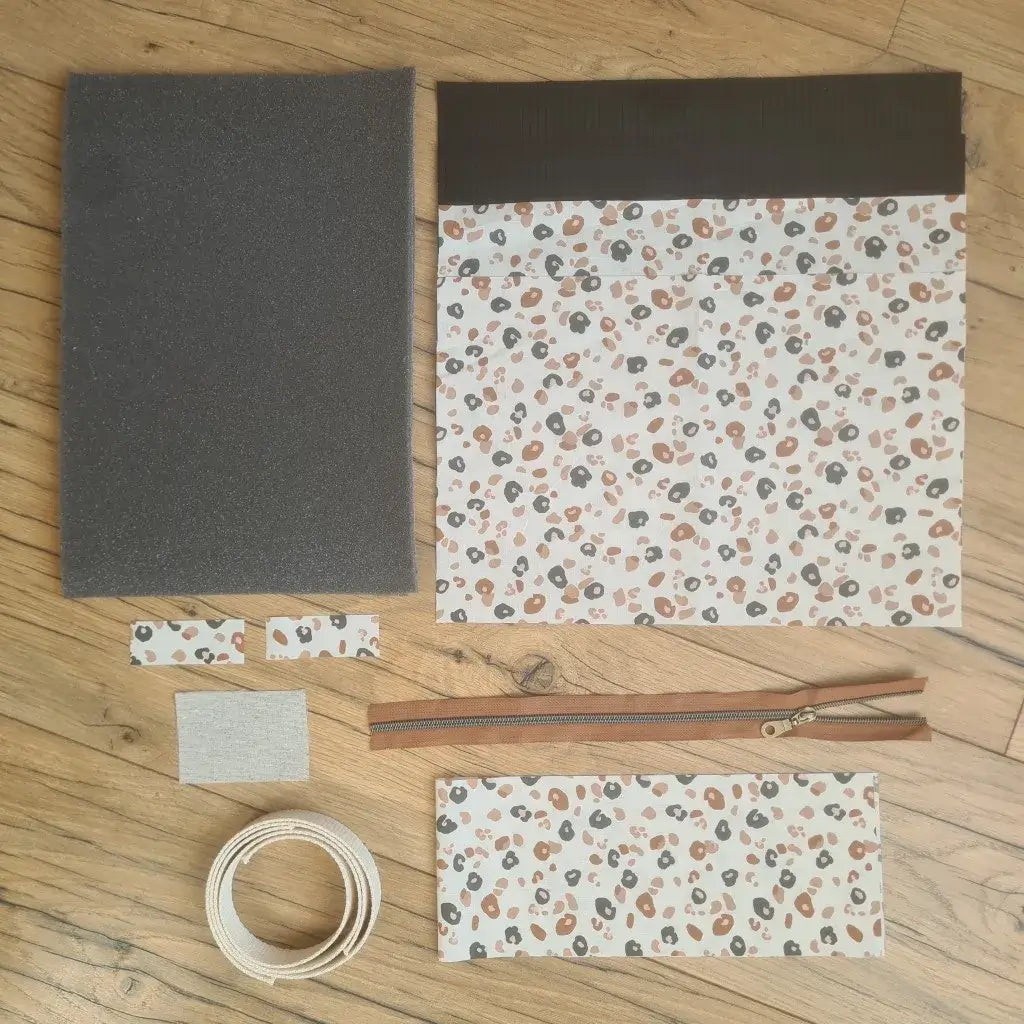 Kit "prêt à coudre" pour réaliser une housse avec anses pour tablette ou iPad en velours côtelé noir doublée avec un tissu à motif léopard. Ce kit couture est composé de 2 plaques en mousse, de 2 pièces en velours côtelé noir, de 5 pièces en coton imprimé à motif léopard, d'une fermeture éclair marron et de 2 sangles. La housse est personnalisable avec un prénom ou une inscription qui peut être floquée sur une étiquette en tissu coton et lin.