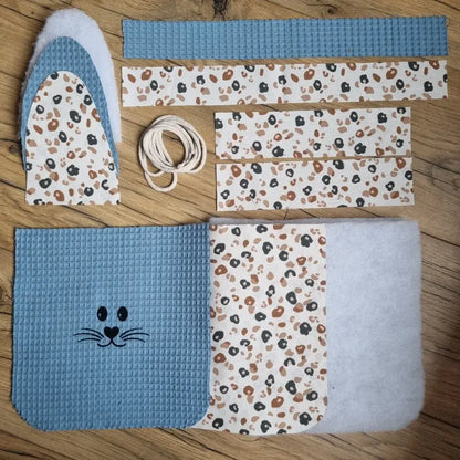 Kit prêt-à-coudre pour réaliser un panier de Pâques molletonné en tissu nid d'abeille bleu denim avec anse. Ce kit est composé de 5 pièces en tissu nid d'abeille, 7 pièces en coton imprimé à motif (ici est présenté le motif léopard), 4 pièces en molleton et de cordelette. Ce kit est personnalisable avec le flocage d'un prénom en option.