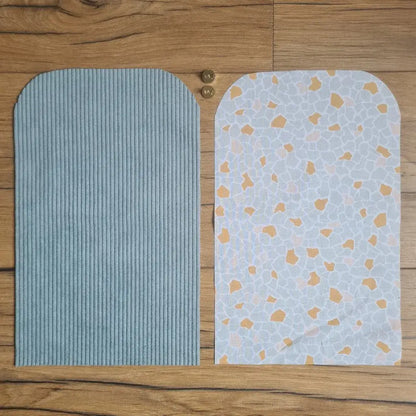 Kit "prêt à coudre" pour une pochette aimantée en velours côtelé au coloris bleu clair avec une doublure en tissu à motif argeo. L'ensemble des pièces de tissu, déjà prédécoupées aux bonnes dimensions, sont disposées au sol. A gauche, une pièce en velours côtelé bleu clair. A droite, une pièce en tissu imprimé à motif argeo. Entre les deux, les 2 pièces composant un bouton aimanté.