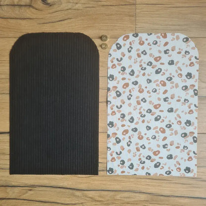 Kit "prêt à coudre" pour une pochette aimantée en velours côtelé au coloris noir avec une doublure en tissu à motif léopard. L'ensemble des pièces de tissu, déjà prédécoupées aux bonnes dimensions, sont disposées au sol. A gauche, une pièce en velours côtelé noir. A droite, une pièce en tissu imprimé à motif léopard. Entre les deux, les 2 pièces composant un bouton aimanté.