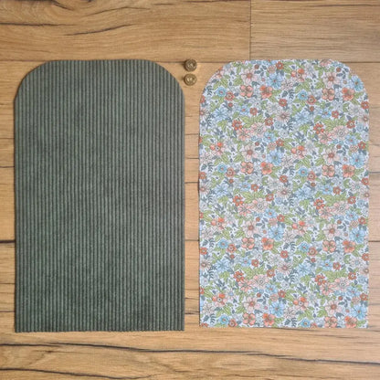 Kit "prêt à coudre" pour une pochette aimantée en velours côtelé au coloris vert avec une doublure en tissu à motif fleurs. L'ensemble des pièces de tissu, déjà prédécoupées aux bonnes dimensions, sont disposées au sol. A gauche, une pièce en velours côtelé vert. A droite, une pièce en tissu imprimé à motif fleurs. Entre les deux, les 2 pièces composant un bouton aimanté.