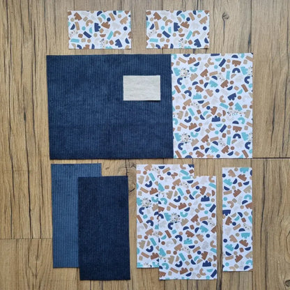 Kit prêt-à-coudre pour protège carnet de santé, composé de tissus prédécoupés avec un motif géométrique bleu et marron, associé à un velours côtelé bleu foncé. Accessoire DIY idéal pour créer un protège carnet unique et personnalisé. Imprimé ludique et moderne avec de petites illustrations d’animaux et de formes abstraites, parfait pour un cadeau de naissance ou pour organiser le carnet de bébé avec style. Kit complet avec toutes les pièces nécessaires pour une couture facile.