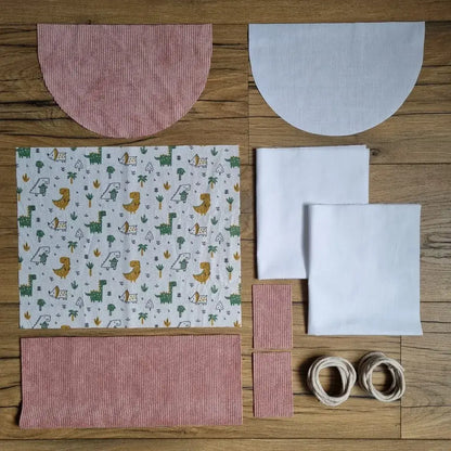 Kit prêt-à-coudre sac à dos pochon personnalisé en velours rose avec rabat demi-lune et tissu imprimé dinosaures, parfait pour un projet couture ludique. 